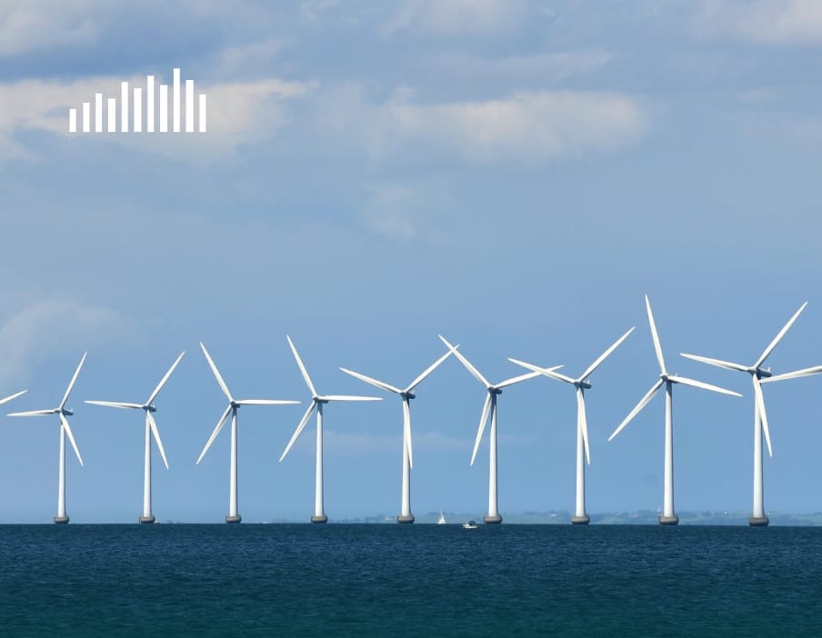 Ni vindmøller står på en række over havet med en blå og lidt overskyet baggrund.